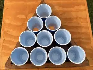 Triângulo de madeira com 10 copos azuis e bolas de ping pong, jogo de beer pong para eventos