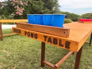 Mesa de beer pong artesanal em madeira com inscrição gravada, disponível para aluguer